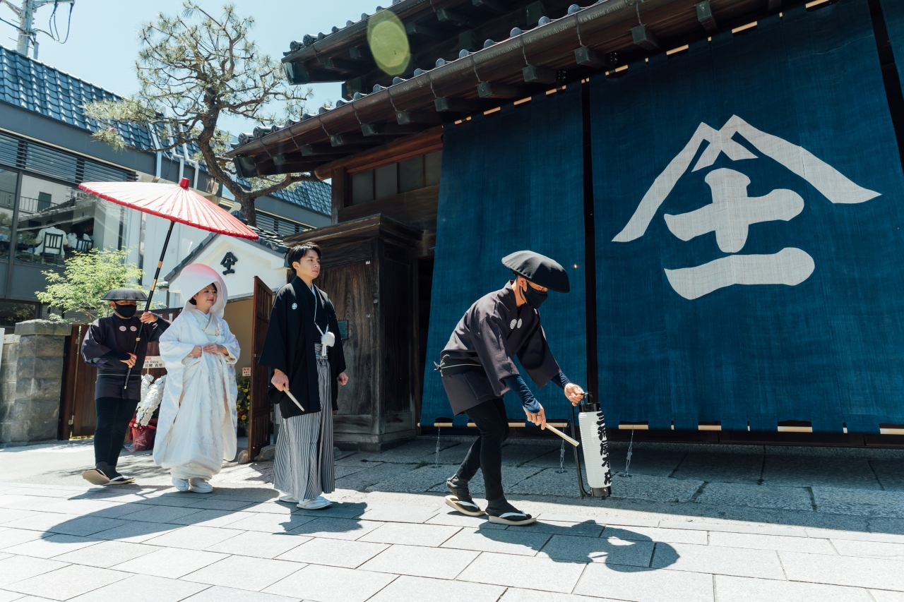三河屋本店の俥夫演出で新郎新婦を赤の大番傘でお供する様子